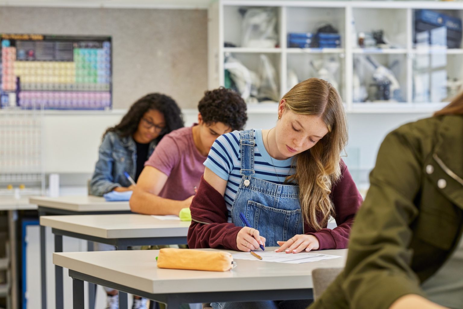 Focused female student complete a multiple choice quiz during classroom test sitting in a row. Multiethnic teenagers working silently while taking a written examination at secondary school. Serious casual girl concentrating on task in academic setting at high school.